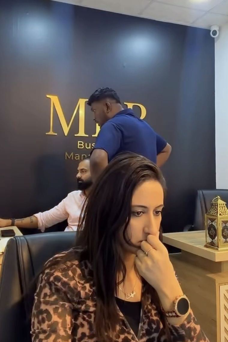 Mehak Butt reviewing a client file at the MKB front desk while the team works behind her