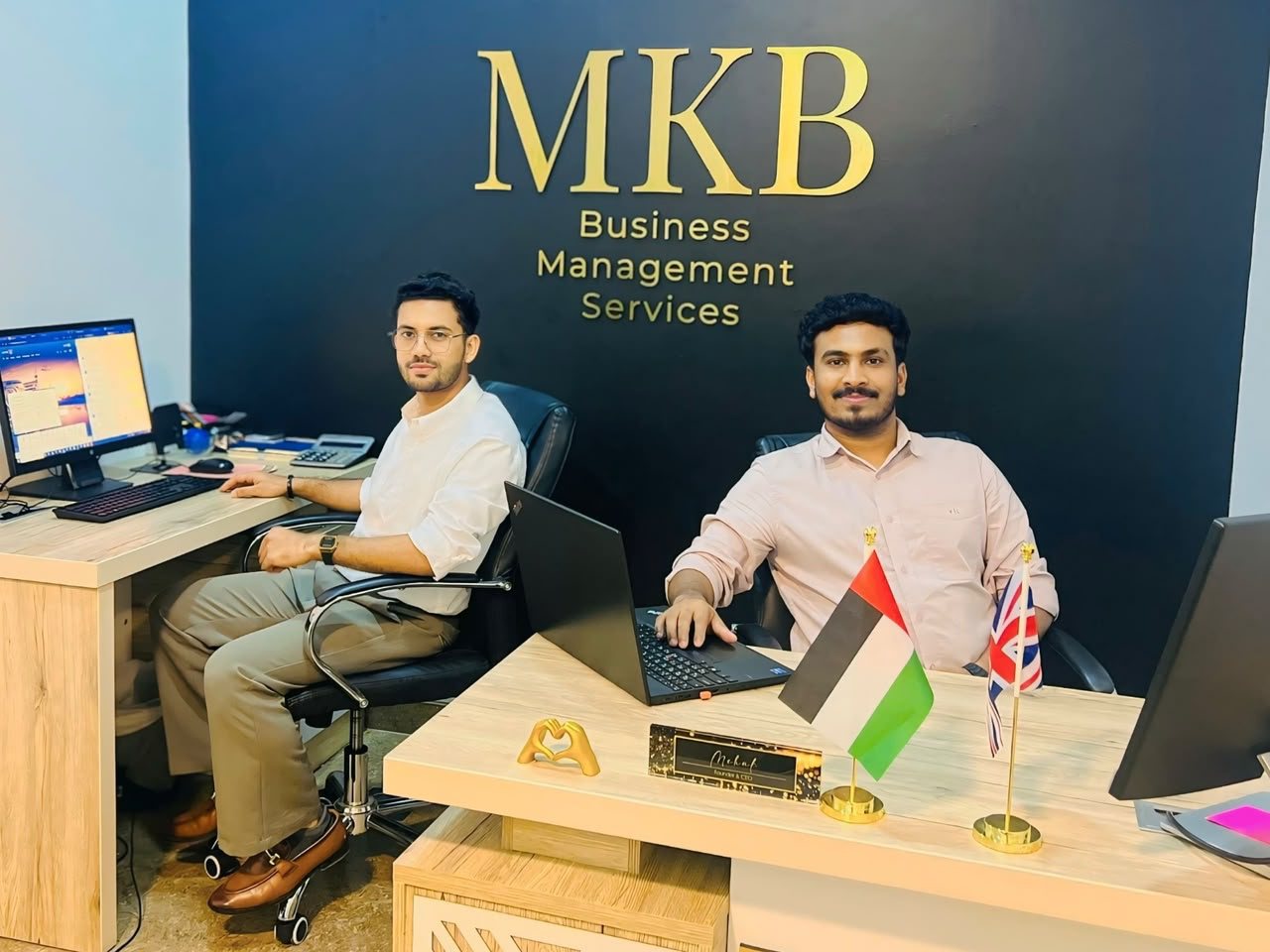 Two members of the MKB team at the front desk beneath the gold MKB logo wall